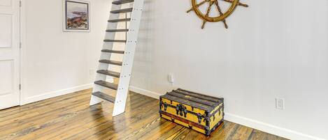 A staircase with a white railing, a wooden ship's wheel on the wall, and a vintage suitcase on the floor.