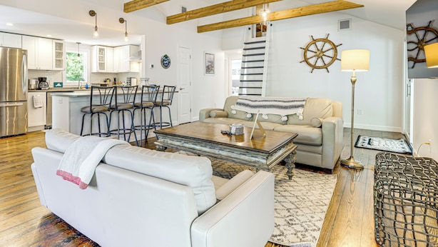 Uma sala de estar moderna com um sofá branco, uma mesa de centro e um espaço de refeições com banquetas.