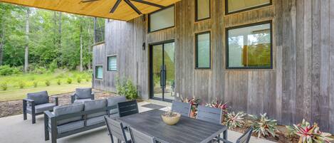 Un patio al aire libre con techo de madera, una mesa y sillas, y vistas a zona boscosa.