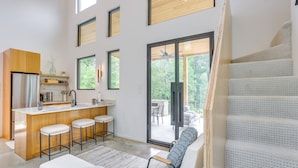 A modern kitchen with a central island, bar stools, and a large sliding glass door leading to an outdoor patio. - 65 Acres: Secluded 'avian Acres' Cabin w/ Pool! (Burkeville)