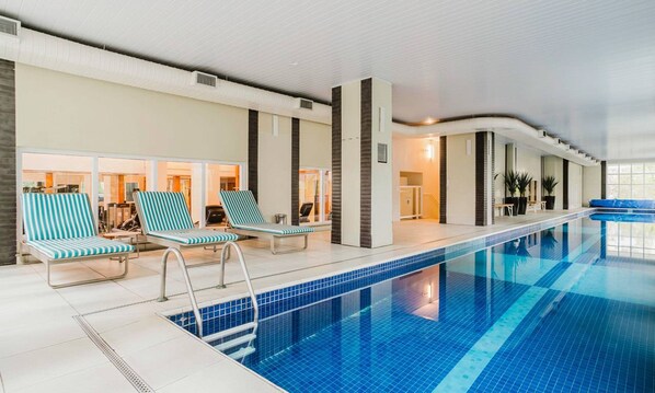 An indoor swimming pool with lounge chairs and a clear view of the pool area.