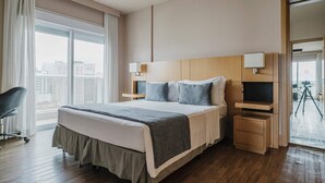 Une chambre d’hôtel moderne, dotée d’un grand lit, d’un bureau avec une lampe et offrant une vue sur la ville par la fenêtre.