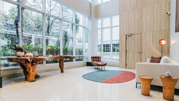 Un vaste espace de vie doté de grandes fenêtres, d’une table basse en bois, d’un fauteuil en cuir, d’un canapé blanc et d’un lampadaire.
