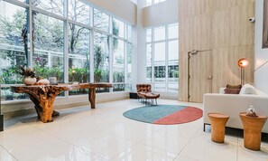 A spacious living area with large windows, a wooden coffee table, a leather armchair, a white sofa, and a floor lamp.