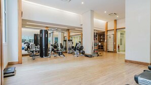 A spacious gym with various exercise equipment, wooden flooring, and large windows.
