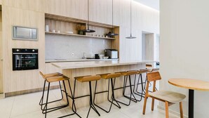 A modern kitchen with wooden cabinets, a built-in oven, a countertop with bar stools, and a dining table.