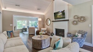 A spacious living room with a fireplace, comfortable seating, and a large TV mounted above it.