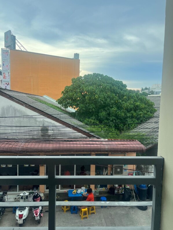 A view of a building with a large tree in the background, a balcony with a table and chairs, and parked scooters. - SK Residence And Restaurant Patong (Patong)