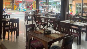 An indoor dining area with wooden tables and chairs, large windows, and a ceiling fan. - SK Residence And Restaurant Patong  (Patong)