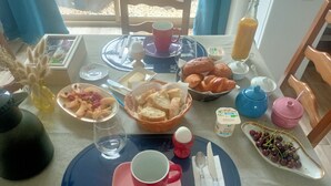A breakfast setting with a table set for two, including plates, cutlery, a teapot, and a variety of food items.
