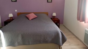 A bedroom with a bed, two bedside tables with lamps, a wooden headboard, and two framed pictures on the walls.