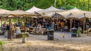 Ein Freiluftmarkt mit Holztischen und -bänken unter großen Zelten, umgeben von Bäumen.