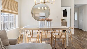 Un coin repas comprenant une table ronde, six chaises, un grand miroir et un lustre.