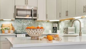 Une cuisine moderne avec des armoires blanches, un four à micro-ondes en acier inoxydable et un saladier rempli d’oranges posé sur le comptoir.