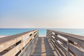 A wooden boardwalk leading to a beach with clear blue water.