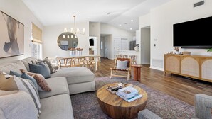 Un salon moderne avec un canapé d’angle, une table basse ronde et un coin repas comprenant une table et des chaises en bois.