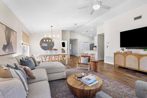 A modern living room with a sectional sofa, a round coffee table, and a dining area with a wooden table and chairs.