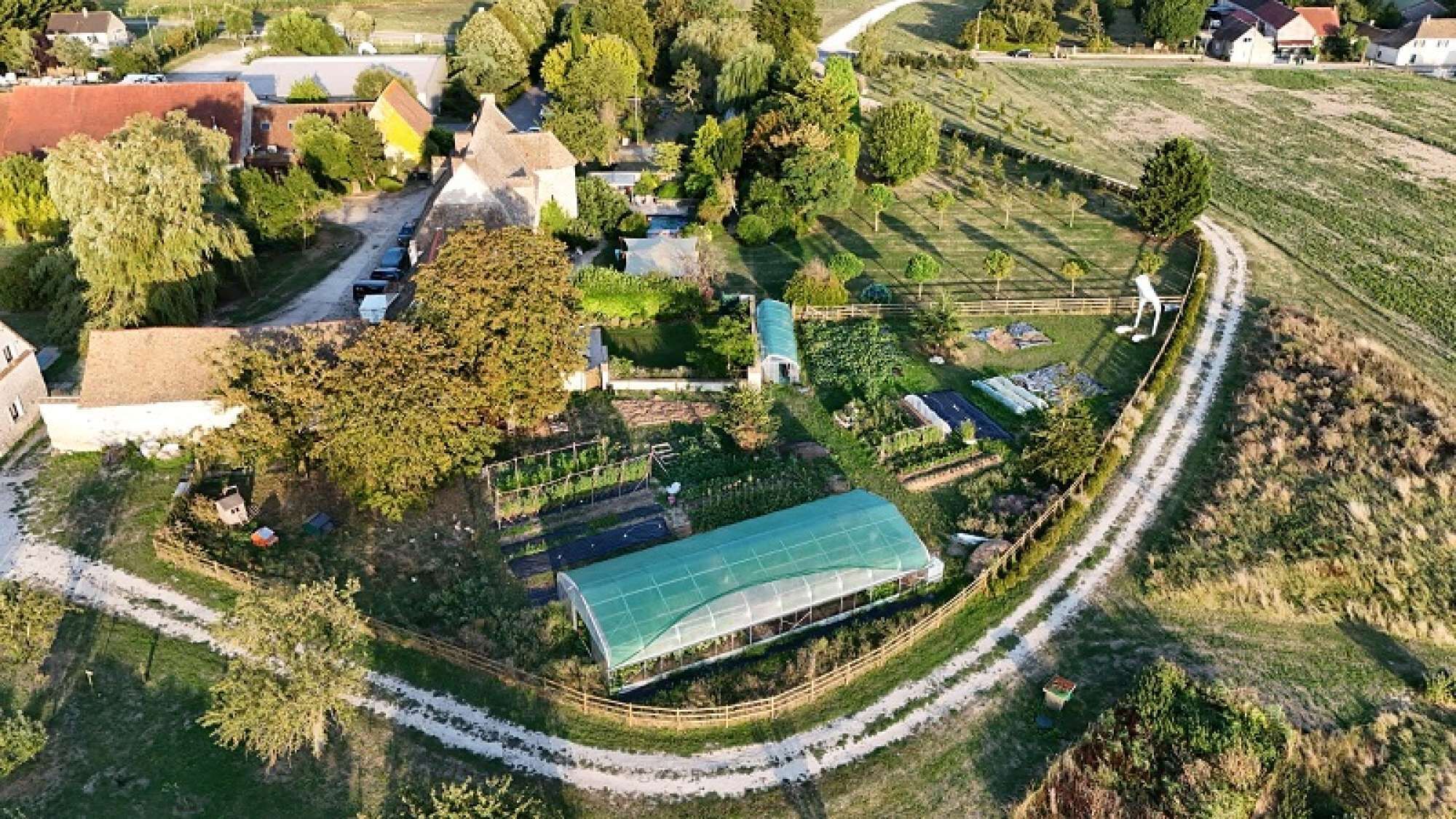 Eine Luftaufnahme eines ländlichen Anwesens mit einem großen Gewächshaus, einem Swimmingpool und einer kurvenreichen Zufahrt.
