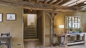 Un intérieur rustique avec des poutres apparentes, un escalier, une machine à coudre ancienne et une petite table agrémentée d’une lampe et d’objets décoratifs.