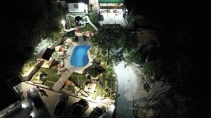 Vista nocturna de una zona residencial con piscina, patio cubierto y una casa con techo verde.
