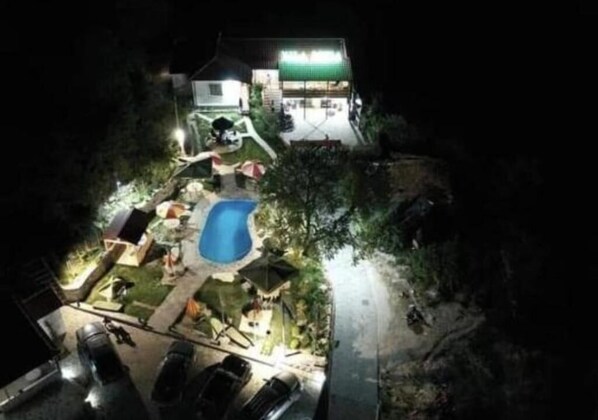 Nattebillede af et boligområde med en swimmingpool, en overdækket terrasse og et hus med grønt tag.