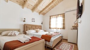 Un dormitorio con dos camas, suelo de madera, televisor montado en la pared y una ventana con cortinas.