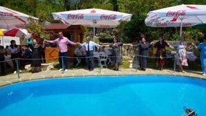 Zona junto a la piscina con sombrillas de Coca-Cola, un muro de piedra y una piscina azul cristalina.
