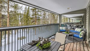 A covered balcony with a view of a snowy forest, a table with a candle and greenery, and a seating area with cushions and a chair. - Minutes from Keystone Resort, come enjoy mountain living! (Keystone)