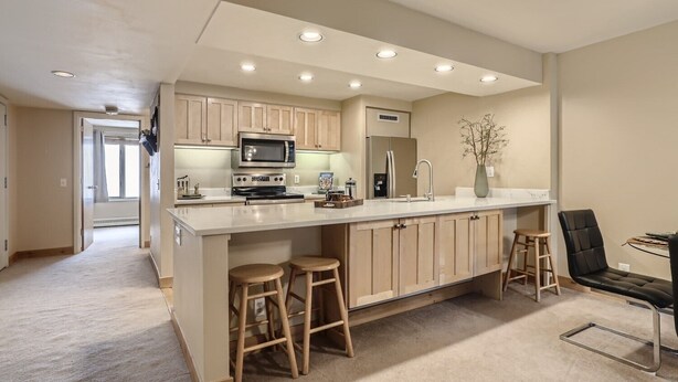 A modern kitchen with a central island, wooden cabinets, stainless steel appliances, and a seating area with stools. - Minutes from Keystone Resort, come enjoy mountain living! (Keystone)