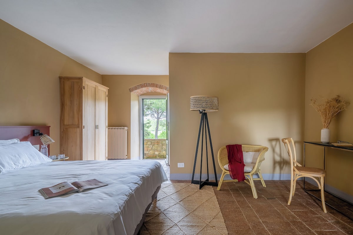Un dormitorio con una cama, un armario de madera, una lámpara de pie, una silla y una mesita.