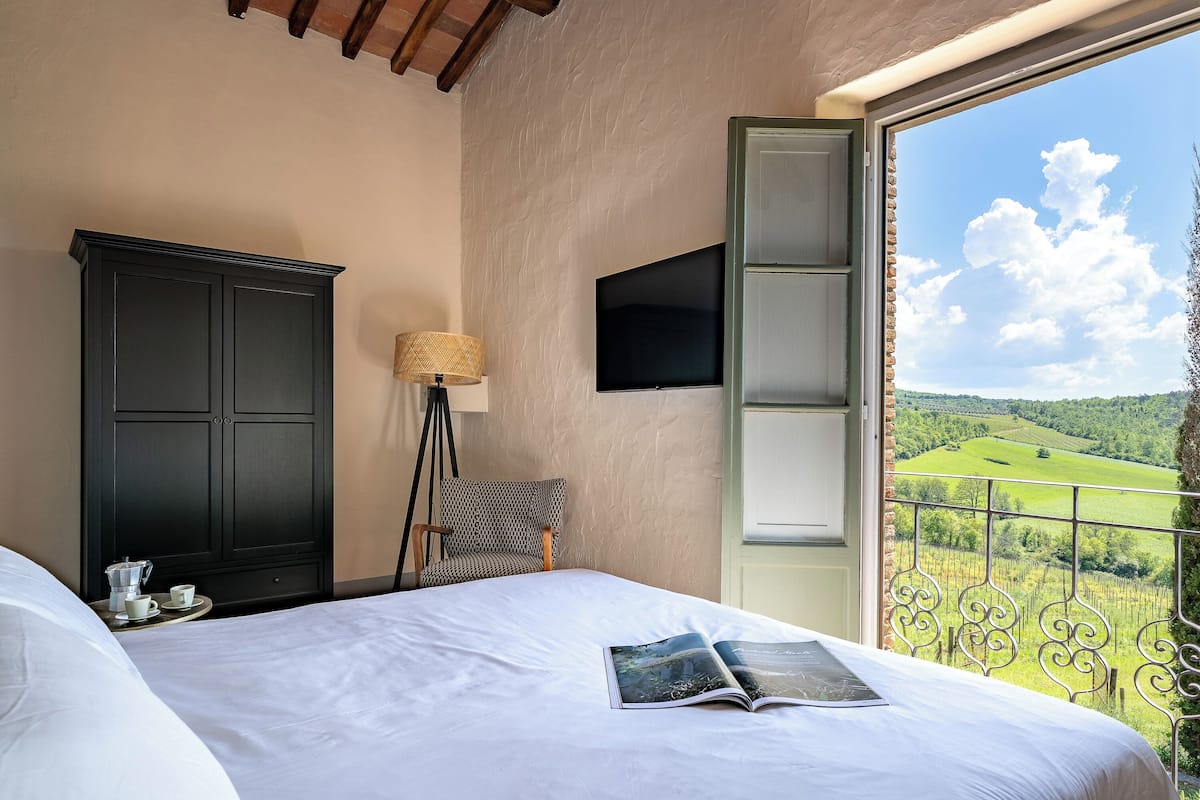 Un dormitorio con cama, armario, televisor, lámpara y balcón con vistas al campo.