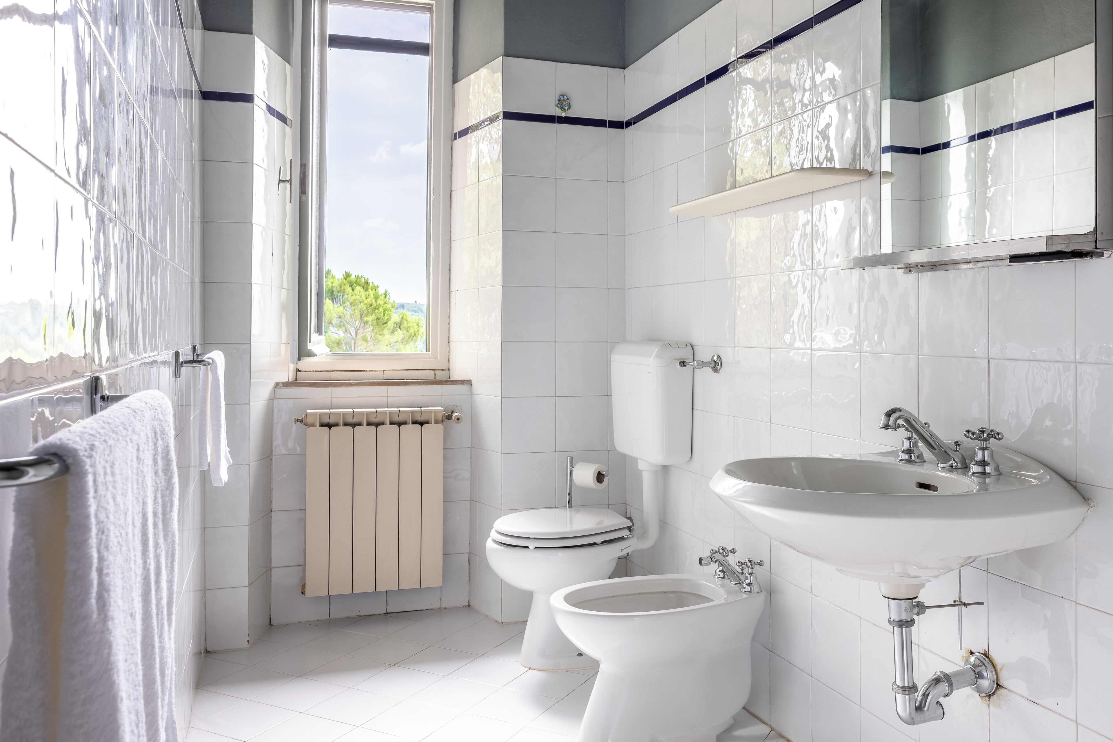 A modern bathroom with white tiles, a toilet, bidet, and a sink.