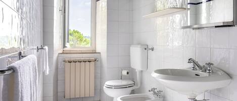 A modern bathroom with white tiles, a toilet, bidet, and a sink.