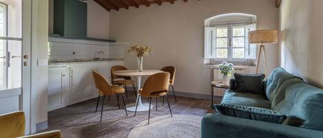 A cozy kitchen with a dining area, featuring a round table, chairs, and a sofa.