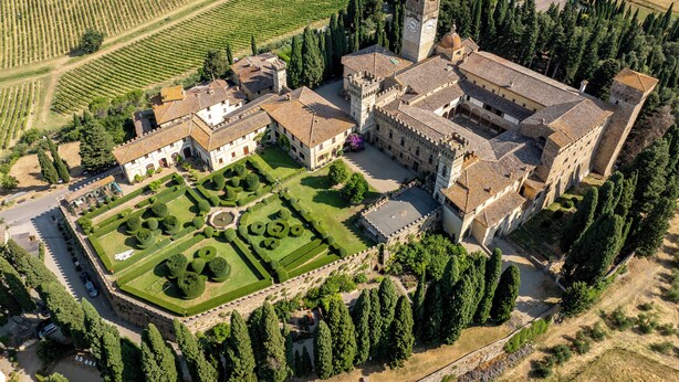 An aerial view of a historic building complex with a central courtyard, surrounded by vineyards and dense trees.