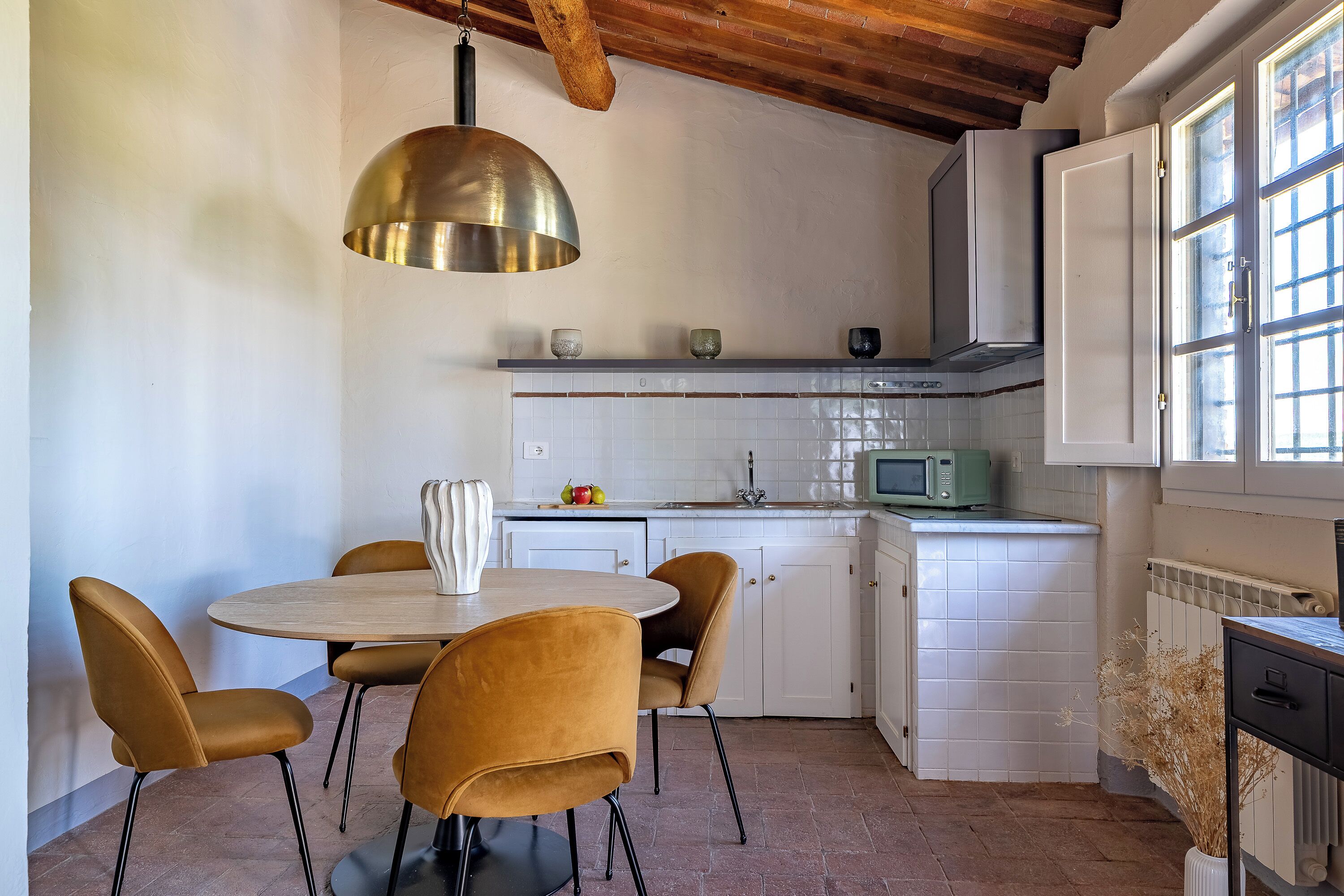 Una cocina con una mesa redonda y cuatro sillas, armarios blancos, un microondas y un ventanal con vistas.