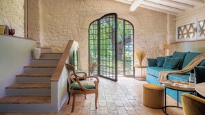 A staircase leading to a room with a stone wall, a green chair, a sofa, and a view through a large window.
