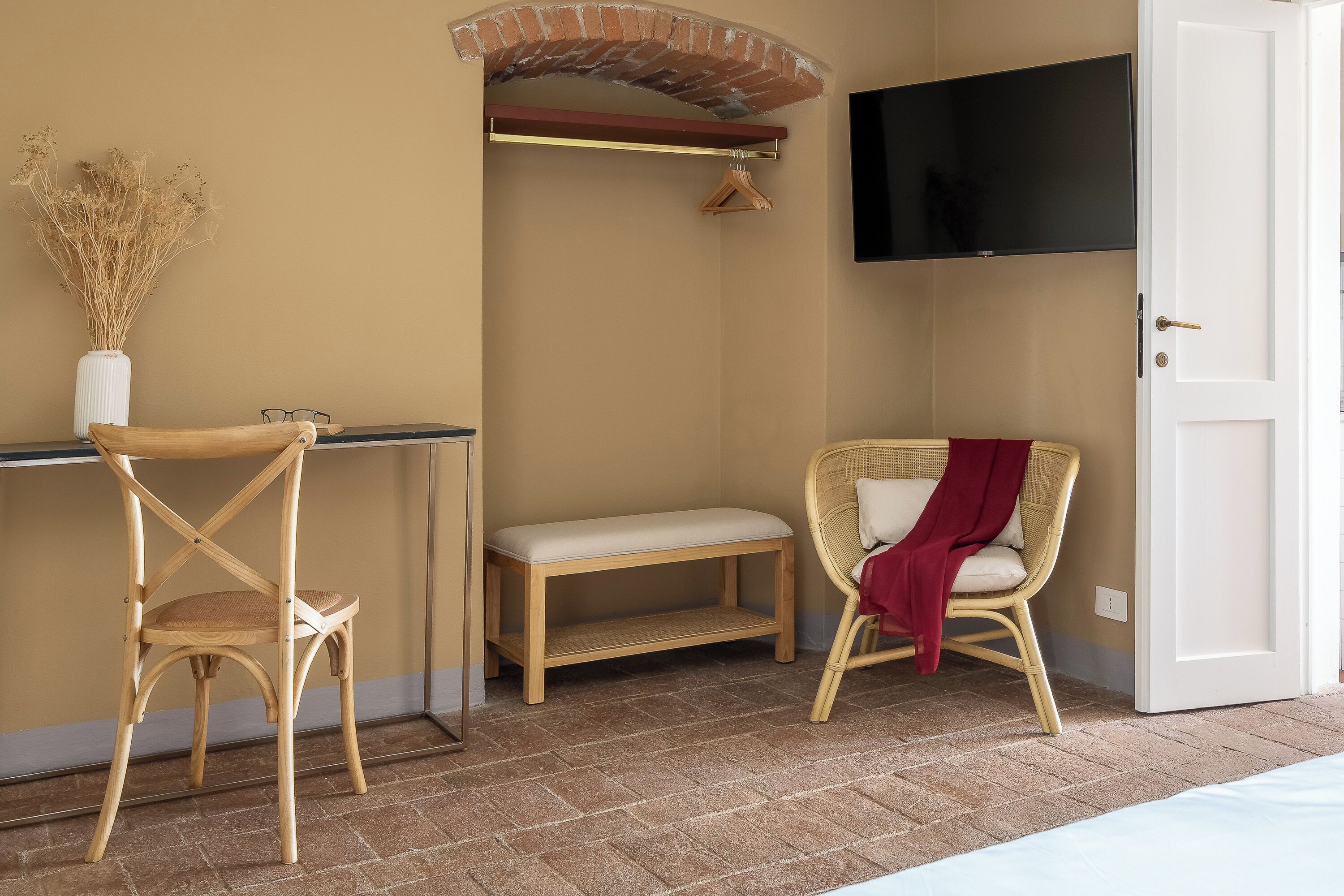 A room with a wooden chair, a bench, a hanging coat rack, a television mounted on the wall, and a door.