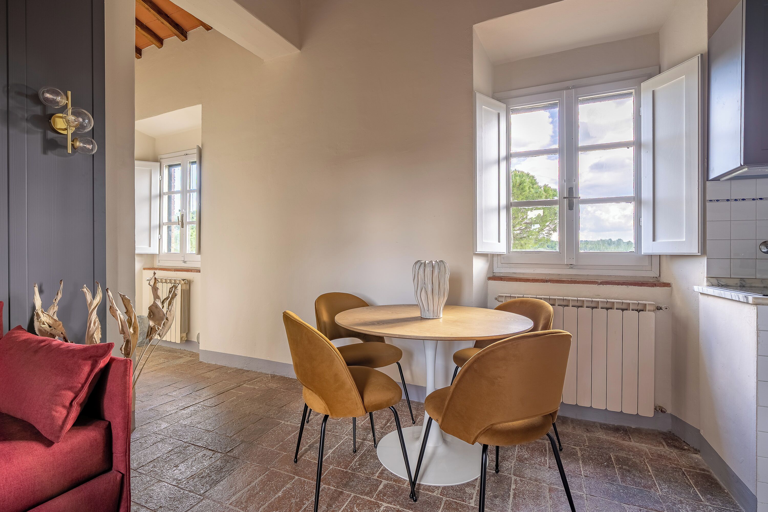 Een moderne keuken met een ronde tafel, vier stoelen, een raam met witte luiken en een radiator.