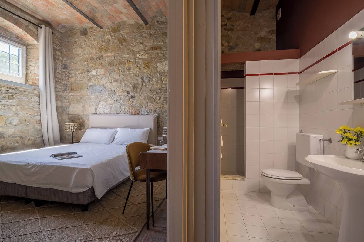 Un dormitorio con pared de piedra, cama, escritorio y silla.