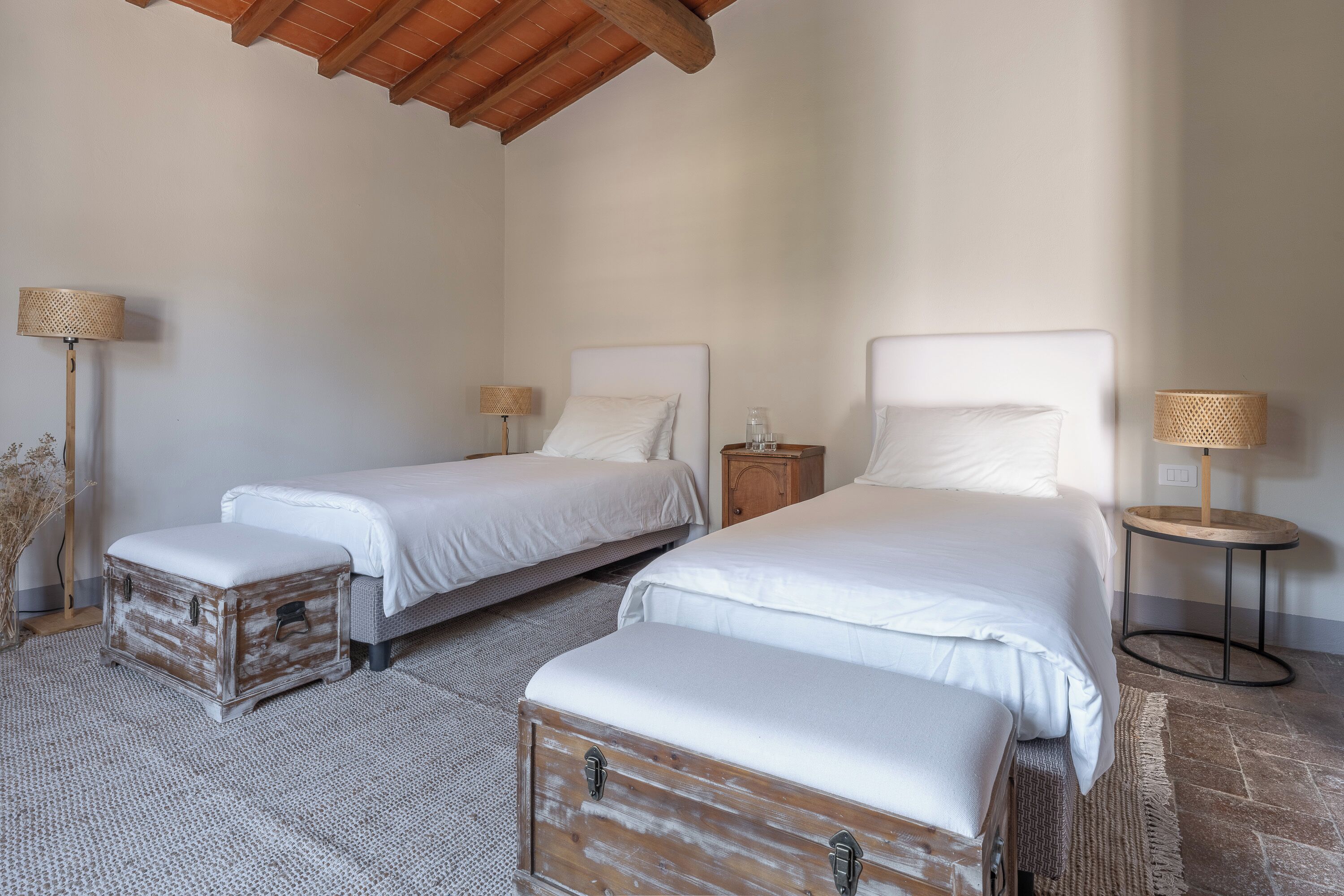 Ein Schlafzimmer mit zwei Betten, einer Holzkiste und einem kleinen runden Tisch mit einer Lampe.