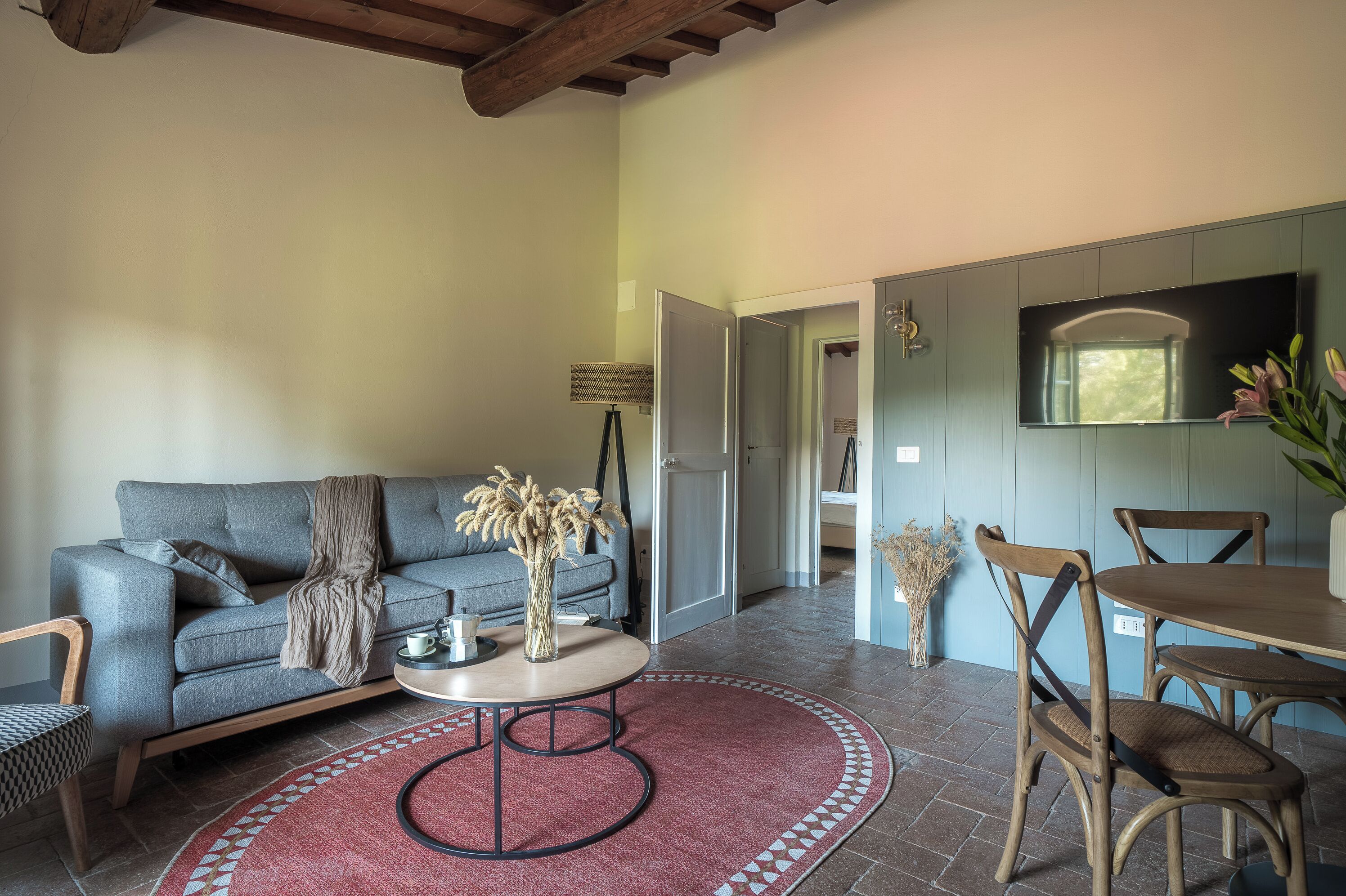 A living room with a sofa, coffee table, and chairs, a TV mounted on the wall, and a door leading to another room.