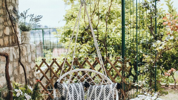 Um jardim com uma cadeira suspensa, um vaso de planta e um muro de pedra.