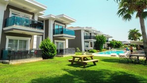 A modern multi-story hotel with balconies, a swimming pool, and a picnic table in the courtyard. - Sweet Home Kemer Apartments (Kemer)