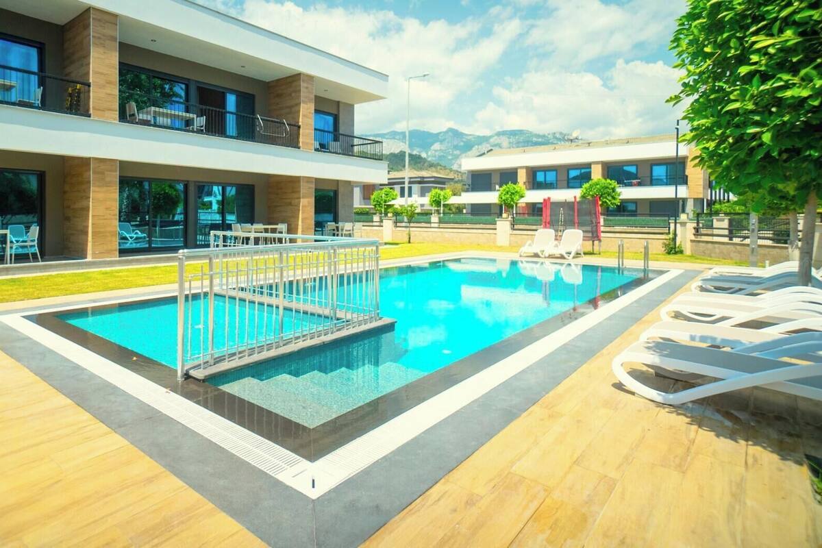 A modern hotel with a swimming pool, outdoor seating, and a view of mountains.