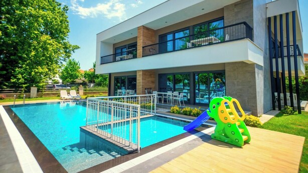 A modern building with a swimming pool, outdoor seating, and a children's play area. - Sweet Home Kemer Apartments (Kemer)