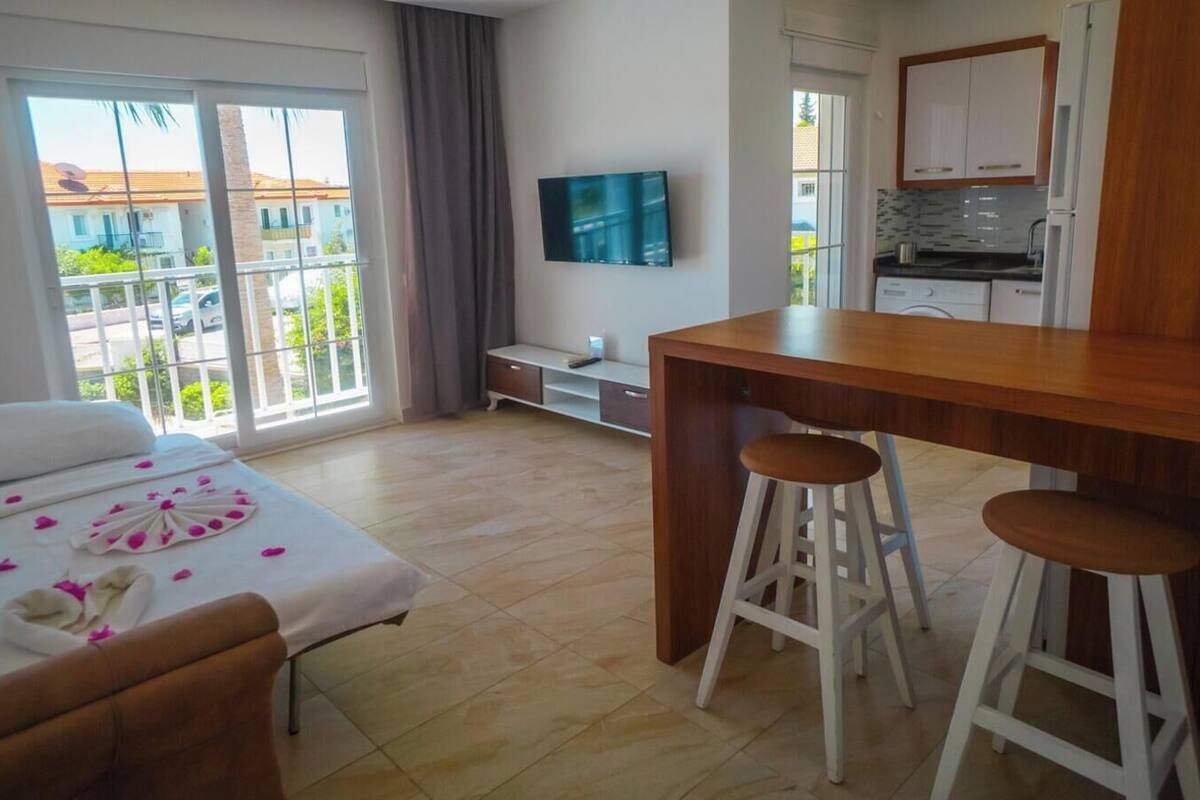 A hotel room with a bed, a dining area with stools, a kitchen, and a balcony with a view.