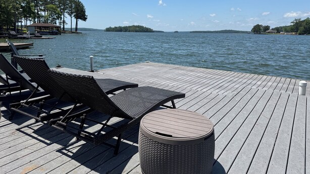 Een houten terras met rieten lounge fauteuils en een vuilnisbak, met uitzicht op een rustig meer met verre eilanden.
