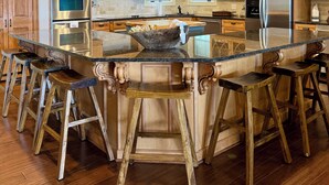 A modern kitchen with wooden cabinets, stainless steel appliances, and a central island with bar stools. - Large Lakehouse. Sleeps 17. Dock. Paddleboard. Flat Lot. Kayaks. Big Lake Views. (Jackson's Gap)