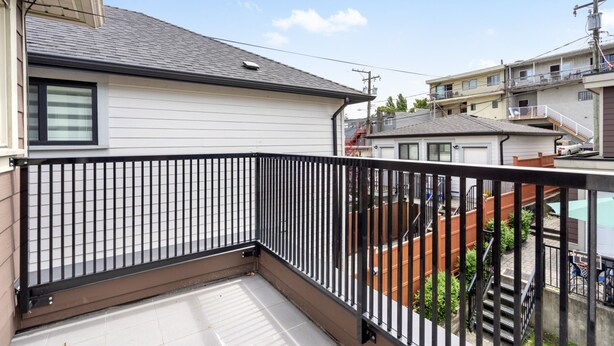 A residential balcony with a black metal railing, a tiled floor, and a view of neighboring houses and a staircase.